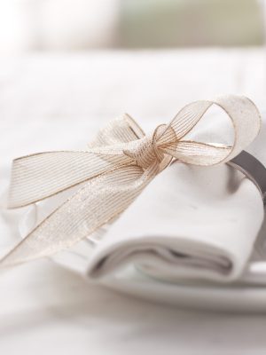 Beautifully elegant decorated table for holiday - wedding or valentine day with modern cutlery, bow, glass, candle and gift, horizontal, closeup, toned