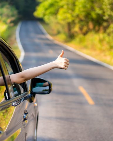 Woman in the car showing her thumb up sign.  Safe driving concept.  Transportation and driving concept and background.